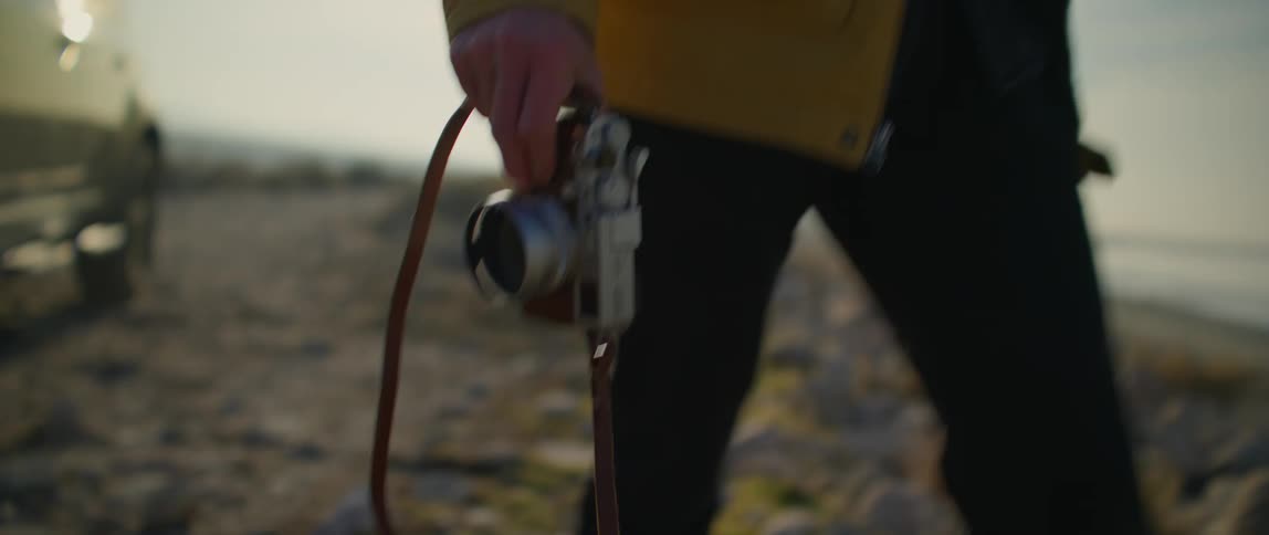 A man walks away from a vehicle in a rural area carrying a camera