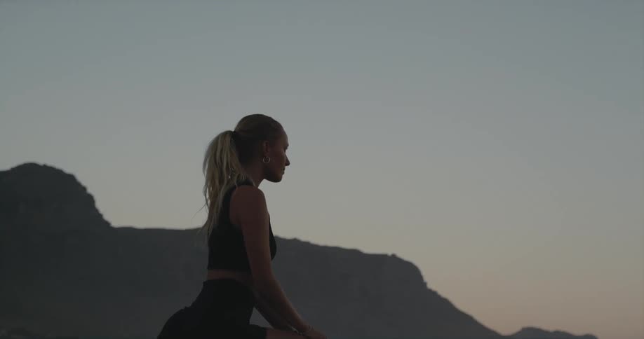 Young blonde woman stretching herself at the beach in front of the ocean during sunset