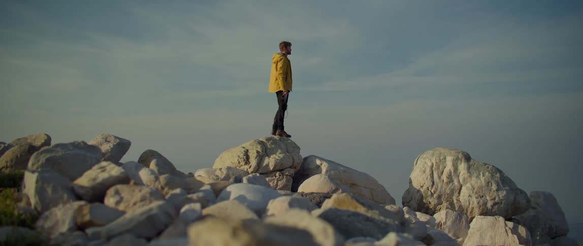 A photographer uses a camera to take a photograph while standing atop a pile of boulders during the day