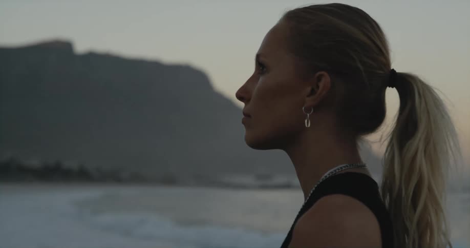 A woman stands on a beach near a mountain and looks around