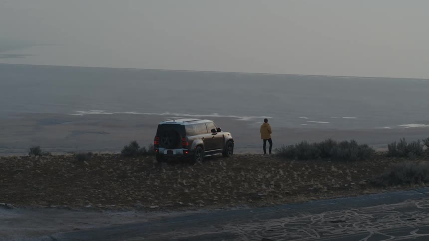A man gets out of his land rover on a ridge overlooking the ocean below and takes a photo