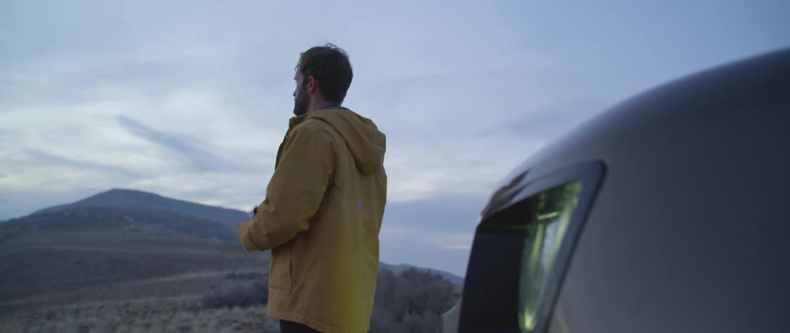 Man standing next to his car in the middle of the nature taking pictures of the rolling hills ahead with his digital camera