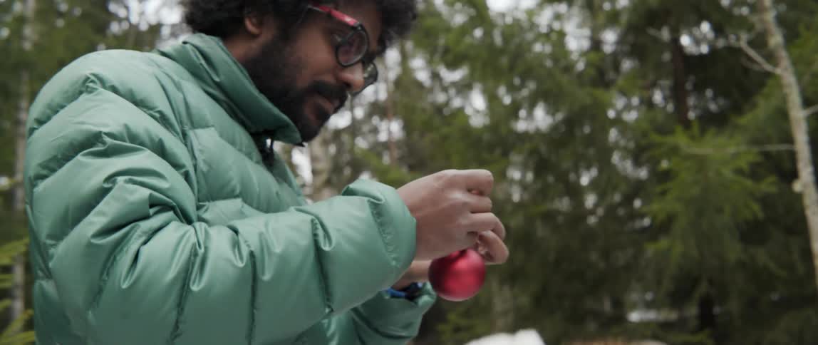 Man and woman tying ornament strings on outdoor tree with joyful holiday energy