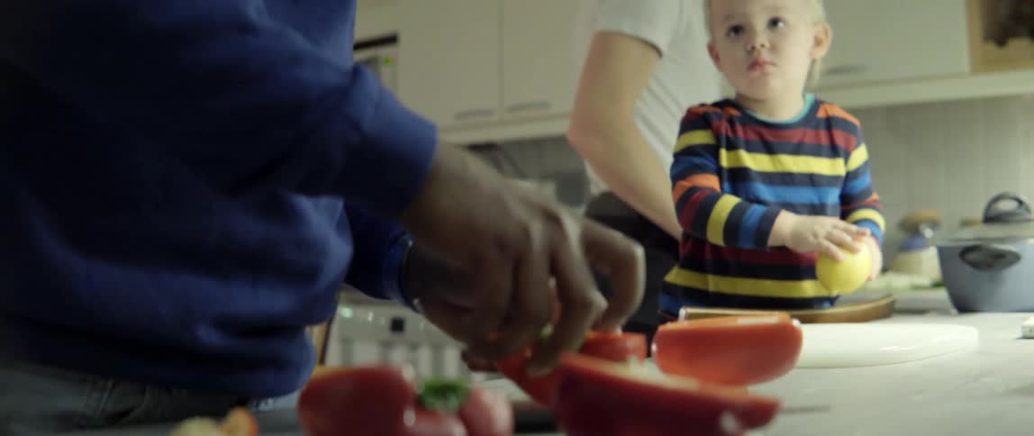 Man preparing healthy organic vegetables in a home kitchen while a young child watches.