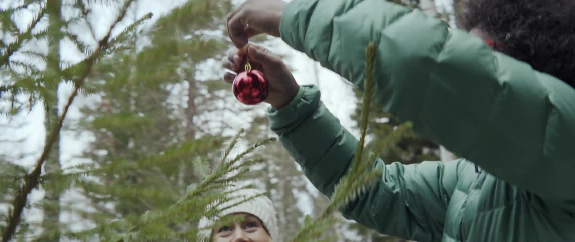 Man and woman hanging Christmas ornaments on outdoor trees with festive joy