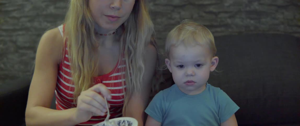 A mother and young toddler sit together eating a healthy snack from a bowl.