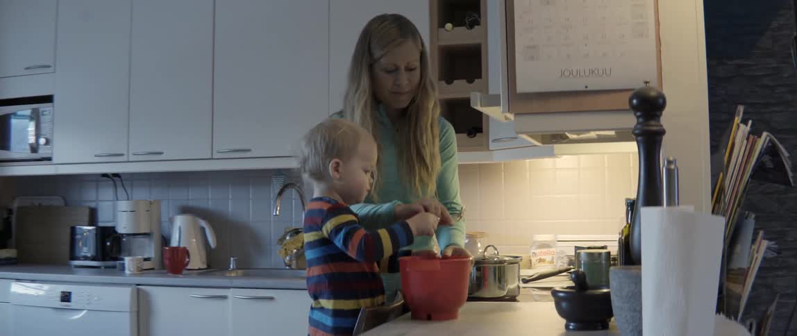 Young mother and small child stirring food while preparing a meal at a counter.