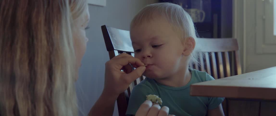 A woman offers a bite of food to her young son at a ta