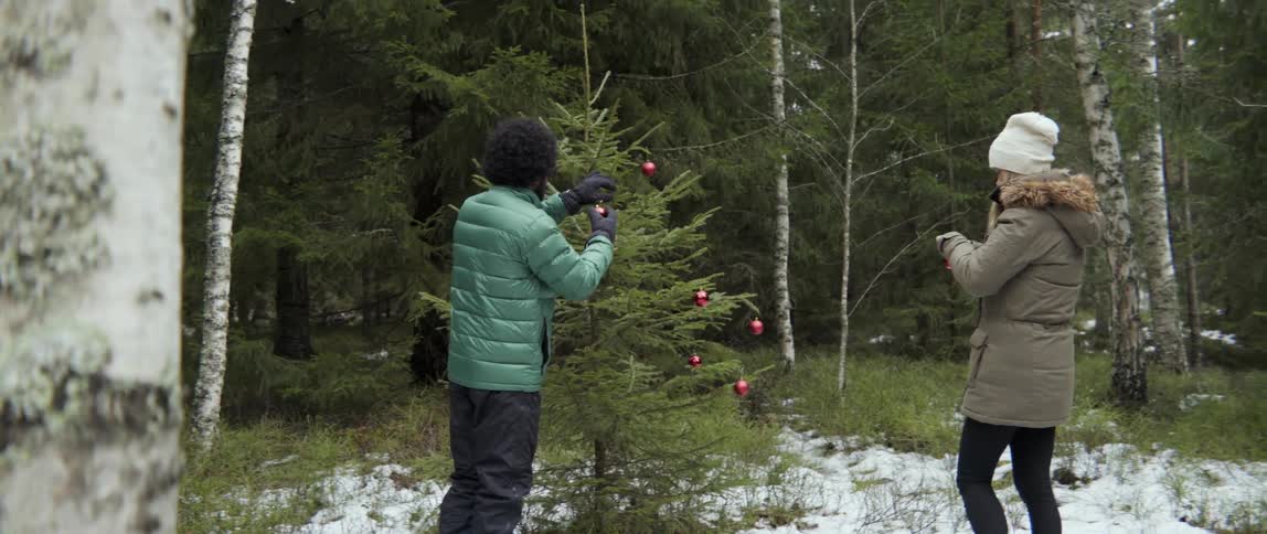 Man placing ornaments on Christmas tree while woman watches with joyful warmth