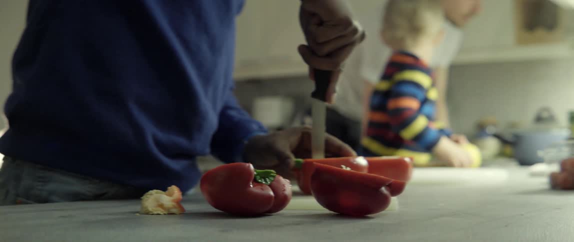 Person cutting fresh red peppers on cutting board with calm kitchen prep.