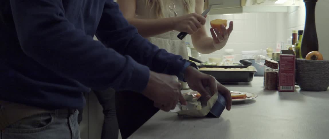 A woman and man cut slices of cheese to place on a plate while standing in a kitchen