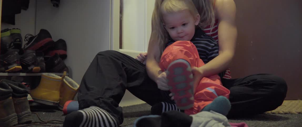Young woman preparing a small child for snow by putting on heavy winter boots.