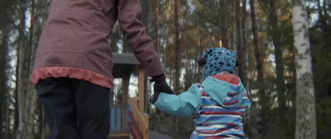 A mother helps her toddler get up off the ground during the day outside