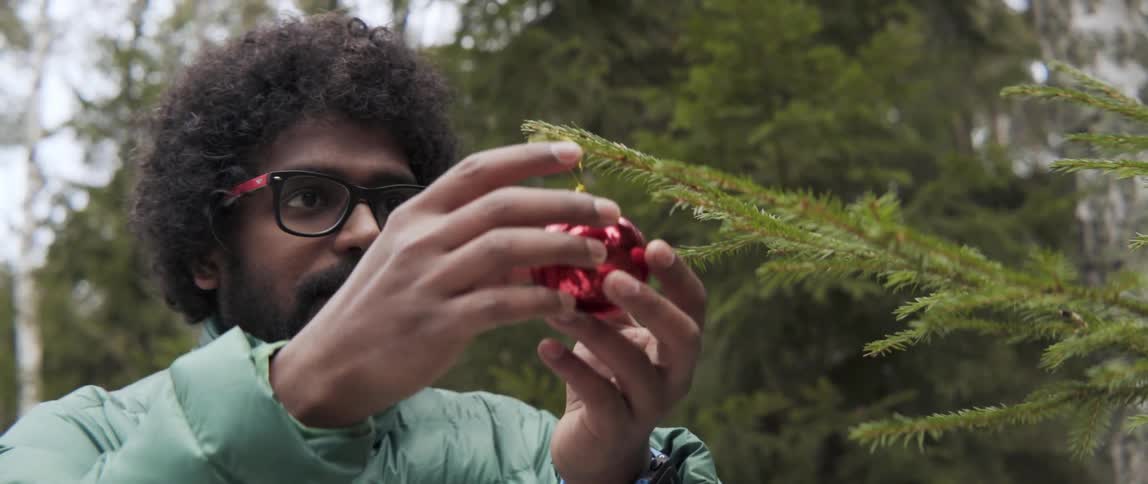 Man hanging Christmas ornament on outdoor tree with festive joyful holiday energy