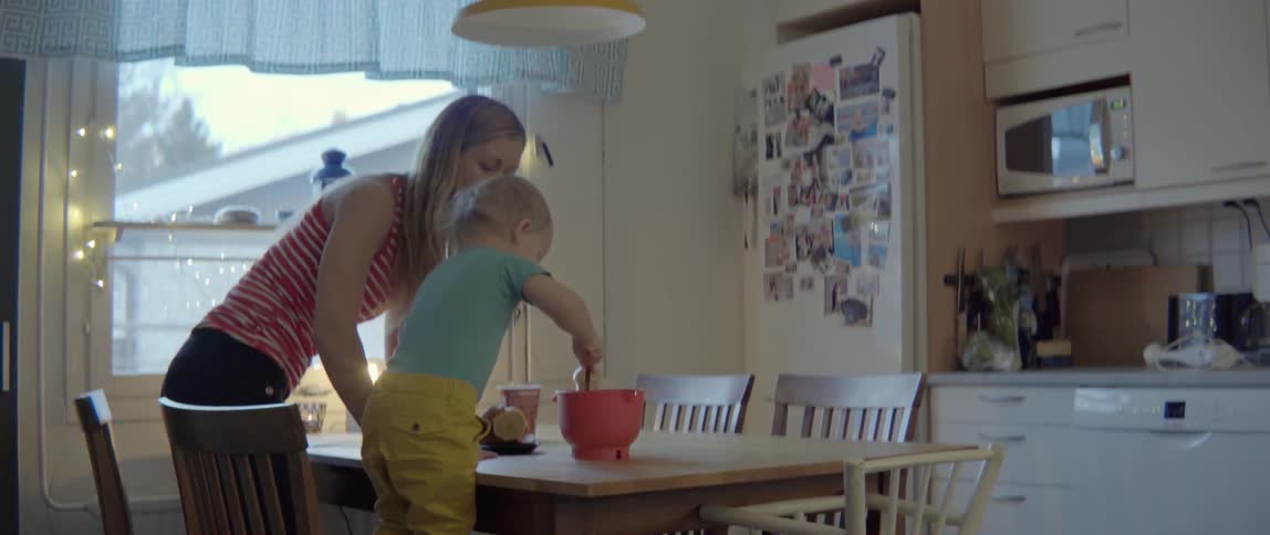 A woman assists her young son as he stirs ingredients in a red bowl.