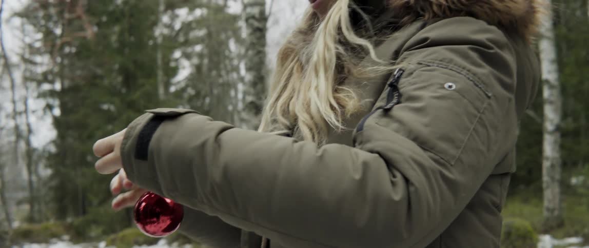 A blonde woman is adjusting a red christmas tree ornament
