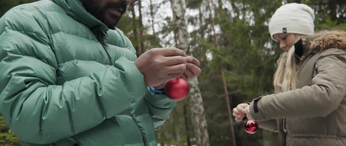 A man and woman hold christmas ornaments in the woods