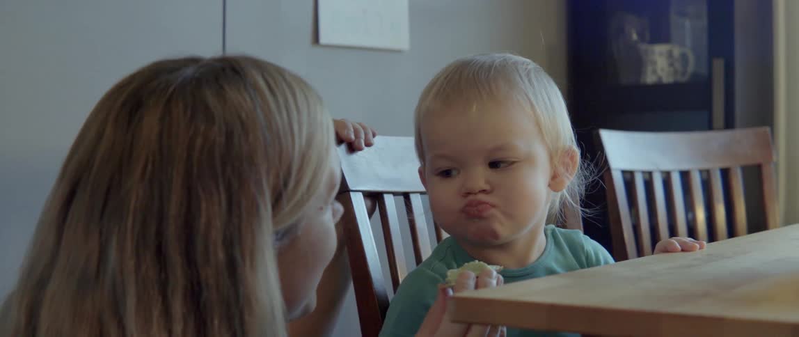 A woman talks to her young son as she feeds him a healthy snack.