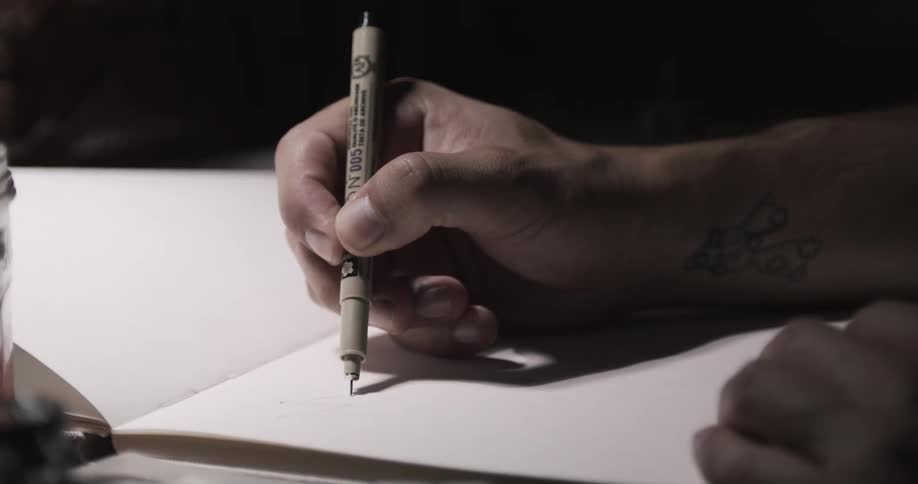 Artist sketches with thin tipped writing utensil in sketchbook