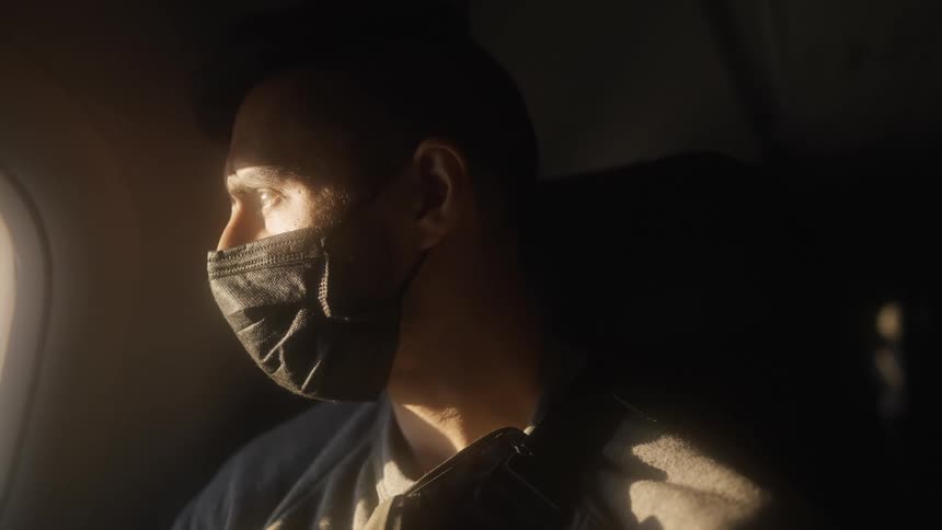 Man wearing facial mask looking out airplane window