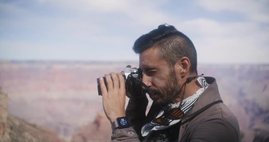 A photographer raises a camera to his eye to take a picture of an immense canyon during the day