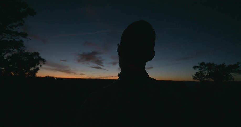 Man watching the horizon is silhouetted against the red sky at dusk