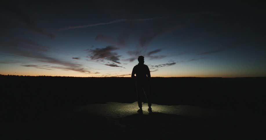 Man stands silhouetted against red tinted horizon at night