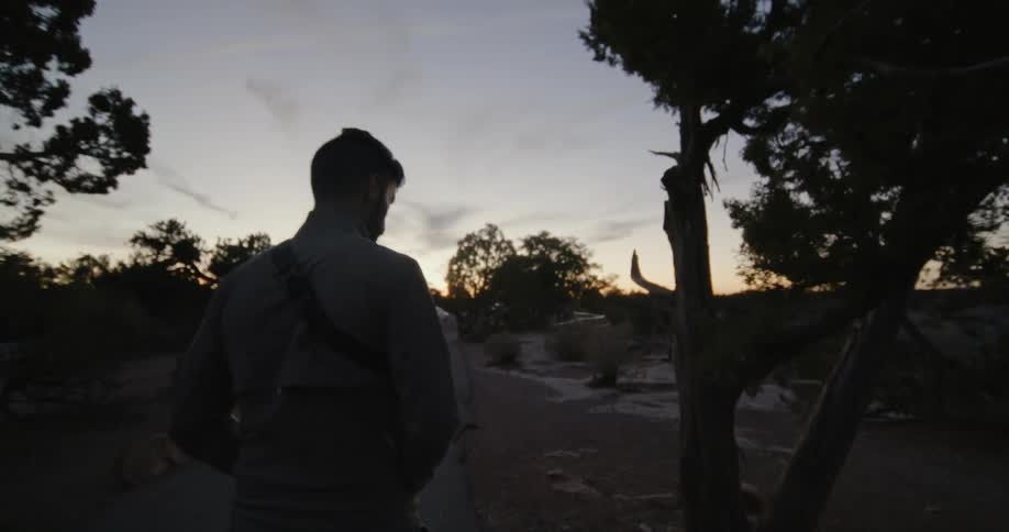A man walks to the edge of a cliff when the sun is low in the sky
