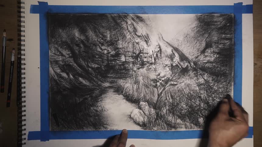 A mans hands as he sketches a picture of a river in a mountain range