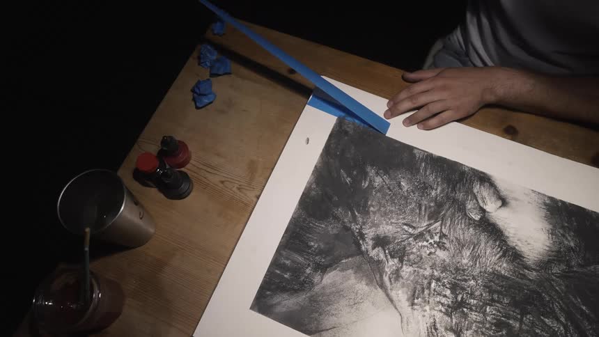An artist removes painters tape from the border of a drawing