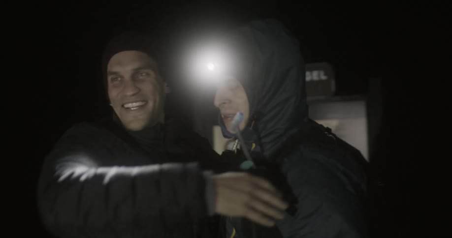 A man hugs another man wearing a bright head lamp