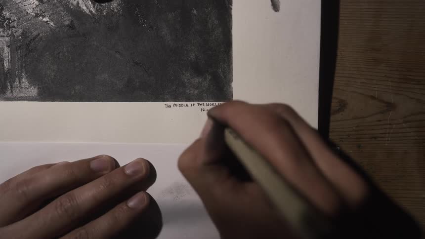 A person signs their charcoal drawing