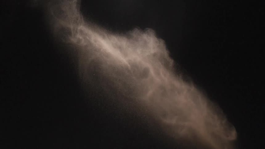 Powder is thrown and dissipates at it falls against a black background