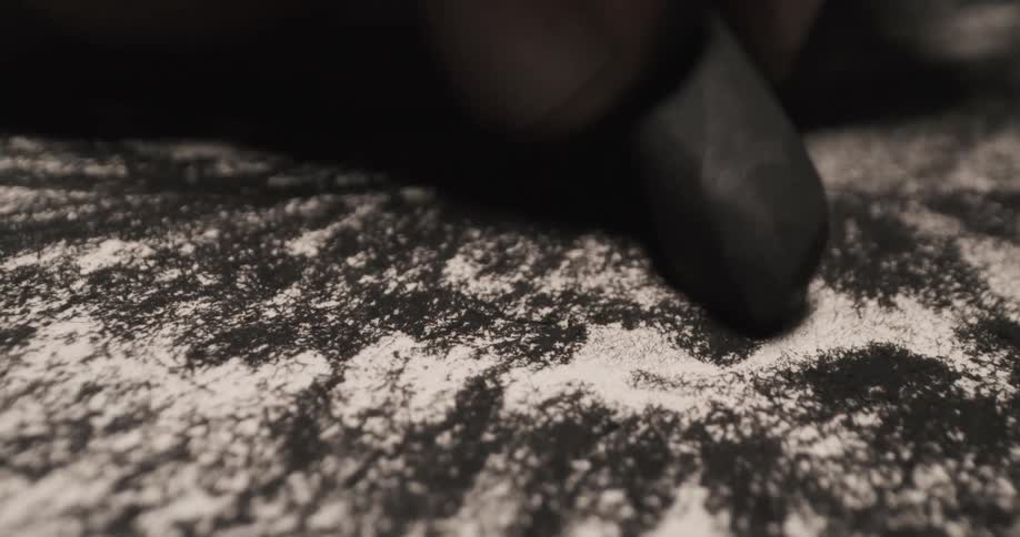 An artist wears a glove while drawing with charcoal on paper
