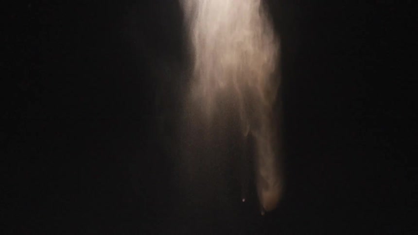 Smoke or chalk flows down then dissipates against a black background