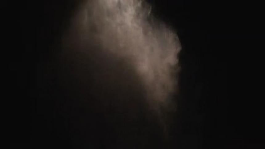 Cloud of white particles dissipates against a black background