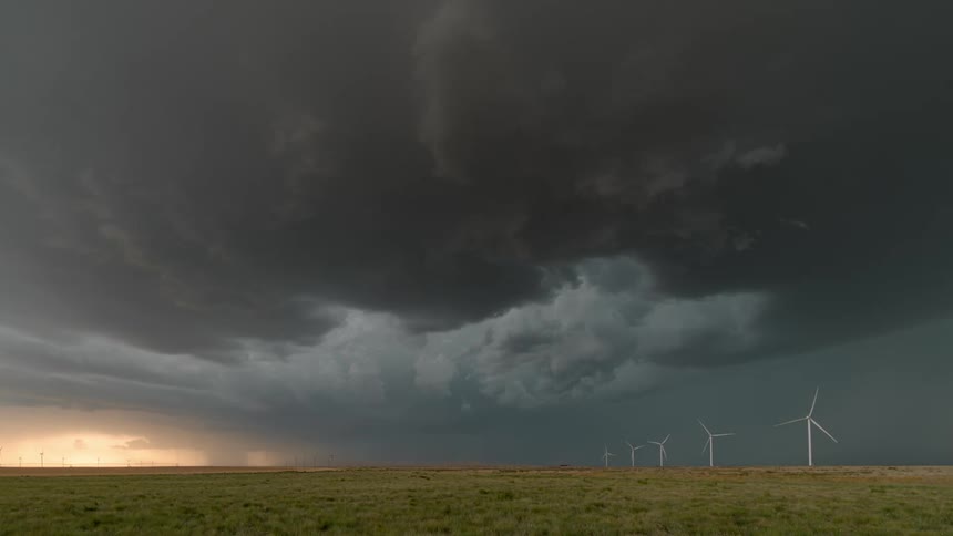 Wind turbines spin on a wind farm under a dark stormy sky