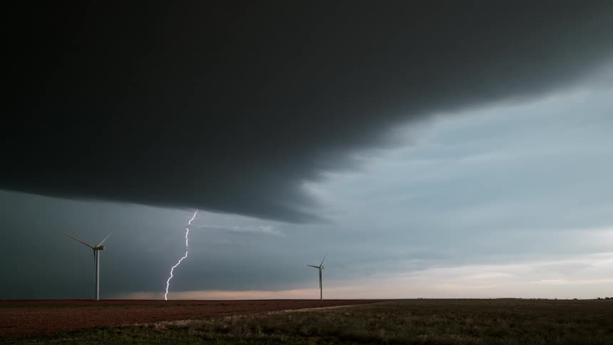 Wind turbines spin as lightning comes down from a dark cloud above