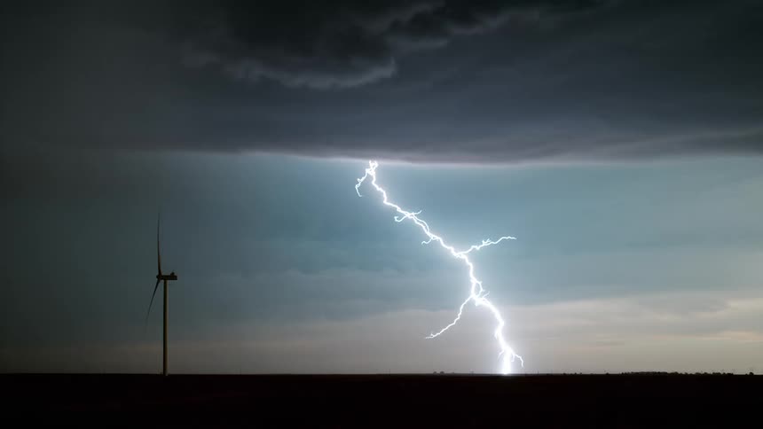 A wind turbine spins as lighting comes down from a dark cloud above