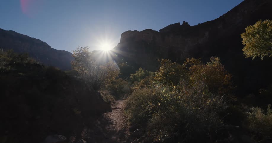 The sun shining over a rocky ridge onto a trail through a canyon