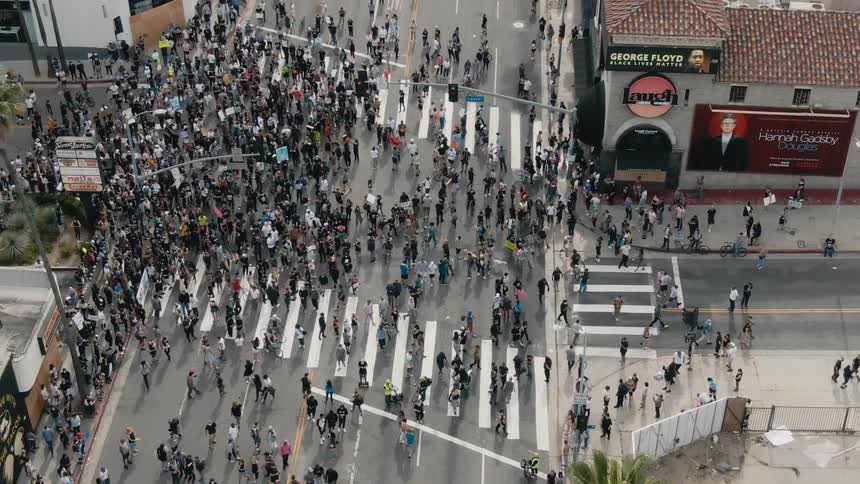 A crowd of protesters occupy a large intersection in a city during the day