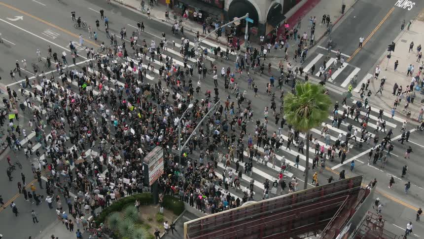 A crowd of people hold a protest in the middle of an intersection in a city during the day