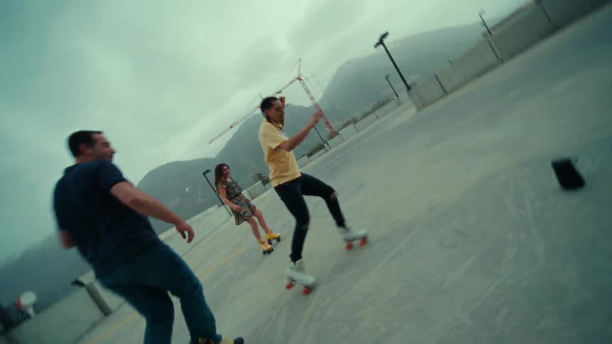A group of people dance while wearing roller skates on the top floor of a parking garage on a cloudy day