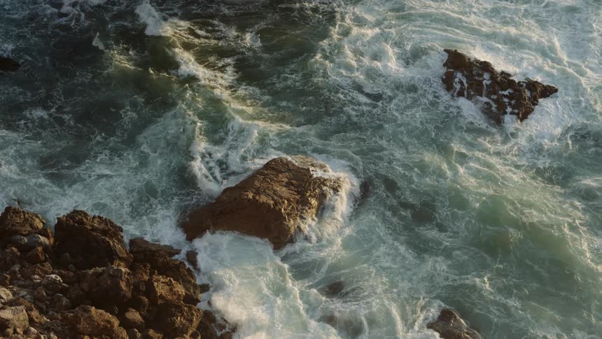 Ocean waves wash over rock formations on the coast during the day