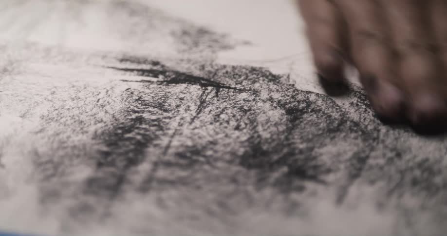 A man uses his hand to blend charcoal chalk on a paper