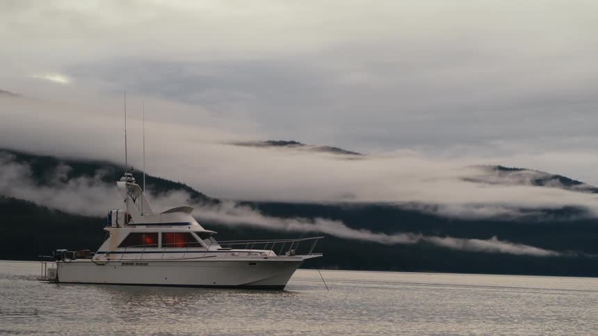A boat anchored in a lake beneath a mountain on a cloudy day