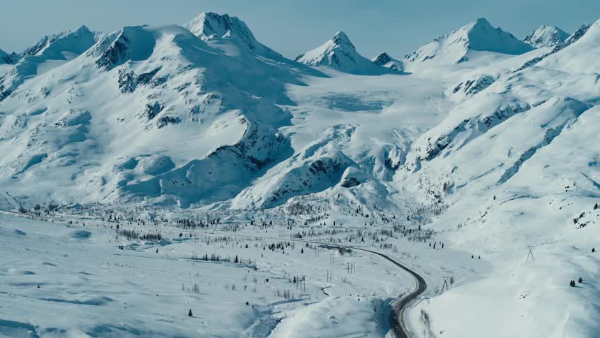 A cleared road winds through a very snowy countryside at the foot of mountains