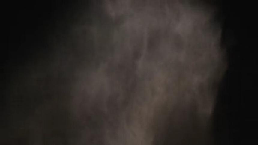 Smoke or dust floats and falls before dissipating against a black background