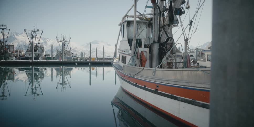 A boat docked in a marina near a snowy mountain range during the day