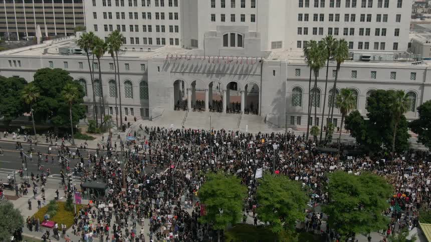 A crowd of protesters stand outside a building as a group of police officers guard the entrance